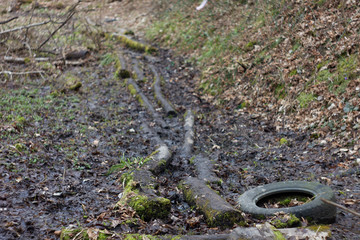 Muddy road in rural path at the forest with creek.