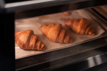 Croissants on a baking sheet are baked in the oven. View through the glass door. Cooking process.