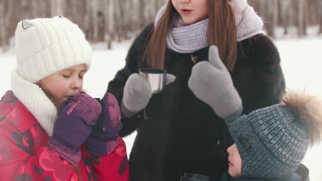 A young woman drinking hot drinks with her children outdoors