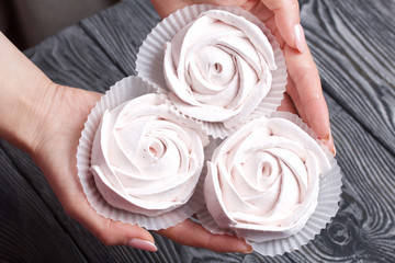 Marshmallows in the form of a rose in the palms of a woman. Against the background of brushed pine boards painted in black and white.