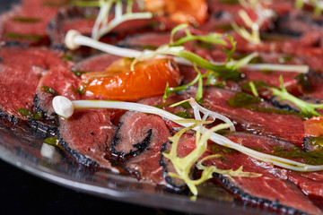 Beef carpaccio with pesto sauce and tomatoes on black table. Restaurant menu, natural and organic food concept.