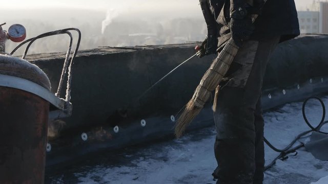 North, Arctic. A worker warms the parapet on the roof with a fire using a propane gas cylinder. The balloon is vaporized