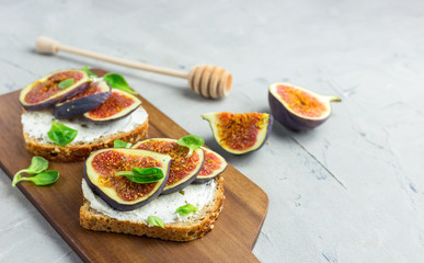 Two Sandwiches with cream cheese, figs, honey and leaves salad served on the wooden rustic cutting board on gray background. Healthy food concept. Top view