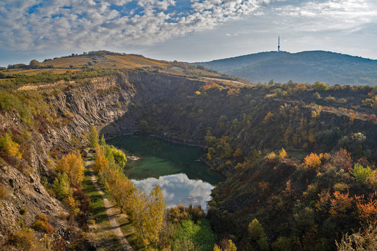 Aerial photo of a lake/quarry pond in the mountains.  Abandoned mine at autumn. Beautiful trees with yellow and orange leaves, warm colors. Tv tower in the background at the top of the mountain.