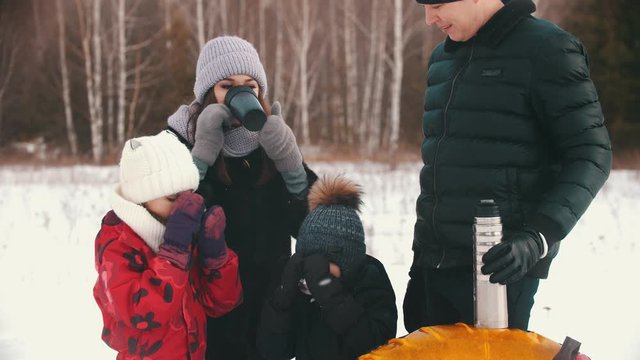 Family drinking hot drinks from the termos near the winter forest