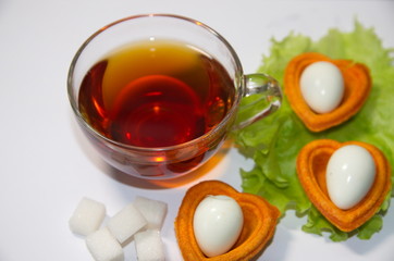 Morning Breakfast. On a white background is a glass cup with black tea, in tartlets are boiled quail eggs and pieces of sugar.