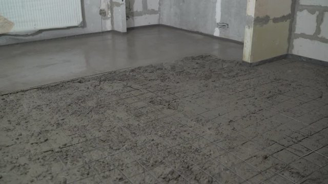 Leveling the floor with a long spatula. Builder levels a laid floor. Floor laying at home. The builder is laying concrete floor in the apartment.