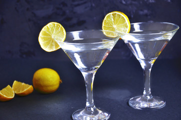 Two glasses of martini with lime on a black background. Two glasses of martini cocktail in a bar