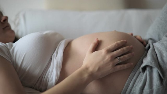 Close-up of the pregnant woman's belly while she's stroking and touching it with her hand at home. Slow motion video