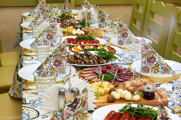 Beautiful served table for wedding or other celebration in restaurant with dishes of cheese, sausage, vegetables (eggplant, tomatoes, bell pepper)