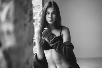 Young brunette in black underwear, knitted knee pads and cardigan sits by the window in a warm blanket