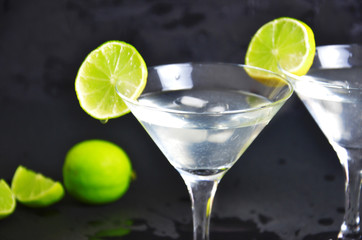Two glasses of martini with lime on a black background. Two glasses of martini cocktail in a bar