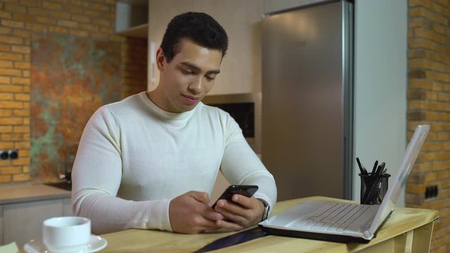 Young male freelancer typing on smartphone, using stock market application