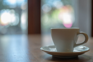 The white ceramic coffee cup with coaster is placed on a brown wooden base on the back, naturally a blurred background.