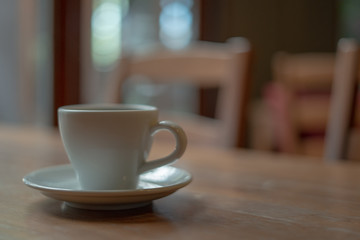 The white ceramic coffee cup with coaster is placed on a brown wooden base on the back, naturally a blurred background.