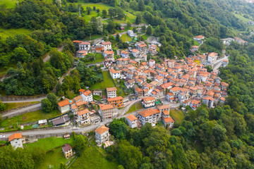 Arial view on mountain Italian village, Garzeno. High angle view of houses with red roofs amoung trees on the top of the mountain in summer.