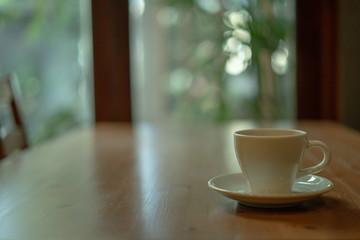 The white ceramic coffee cup with coaster is placed on a brown wooden base on the back, naturally a blurred background.