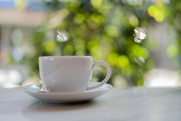 The white ceramic coffee cup with coaster is placed on a brown wooden base on the back, naturally a blurred background.