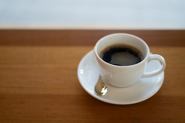 The white ceramic coffee cup with coaster is placed on a brown wooden base on the back, naturally a blurred background.