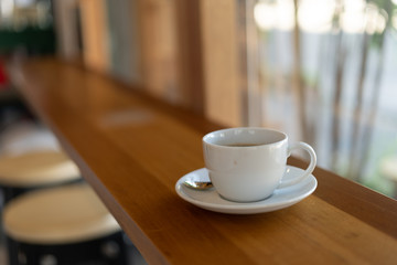 The white ceramic coffee cup with coaster is placed on a brown wooden base on the back, naturally a blurred background.