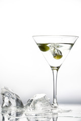 A wine glass of martini and green olives, and pieces of melting ice