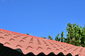 techo de teja roja con fondo de cielo azul y arbol de hojas verdes