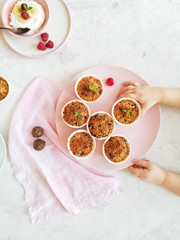 Muffins on a pink plate and cottage cheese with berries and banana on a round plate, served on a light background top view. Children's hands in the frame take the dessert.