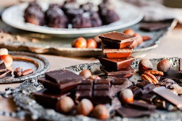 Different kind of delicious organic pieces of chocolate put in a stack. Vintage kitchen tableware, nuts as decor. Close up, macro, front view