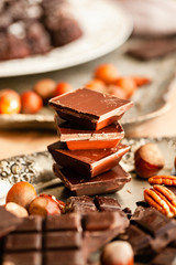 Different kind of delicious organic pieces of chocolate put in a stack. Vintage kitchen tableware, nuts as decor. Close up, macro, front view