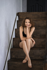 Obraz na płótnie Canvas Beautiful girl in black bikini sitting on wooden stairs at home