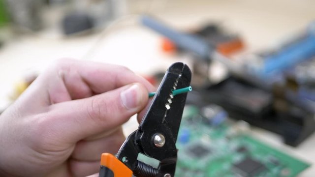 Master cleans insulation on wire with pliers. Workplace with electronic components in electronics workshop. Repair Shop and Electronic Devices Concept