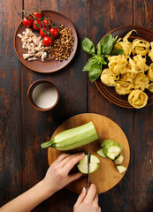 The concept of Italian cuisine. Pasta with zucchini and cheese on a dark wooden background. Cooking process with hands