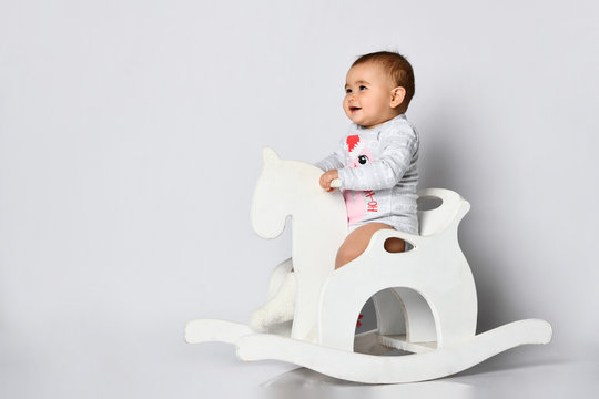 Toddler in gray bodysuit with christmas flamingo print. She riding rocking horse isolated on white. Holidays. Close up, copy space