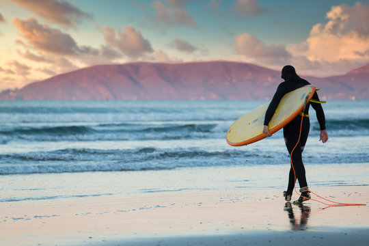 Lone surfer walks into the ocean at dawn in Pismo Beach