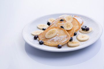 pancakes with banana and blueberries on a white plate, tasty and beautiful on a white background