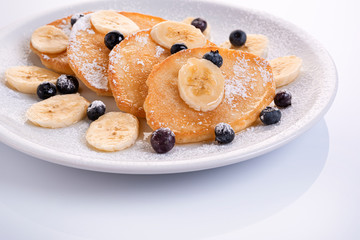pancakes with banana and blueberries on a white plate, tasty and beautiful on a white background