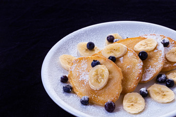 pancakes with banana and blueberries on a white plate, tasty and beautiful on a black background