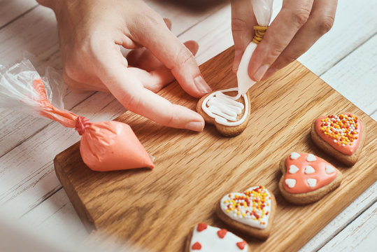 Decorating gingerbread cookies with icing. Woman hand decorate cookies in shape of heart, closeup