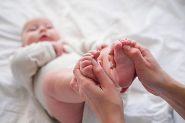 Baby feets in mother hands. Young caucasian woman makes massage for happy infant baby on white bed...