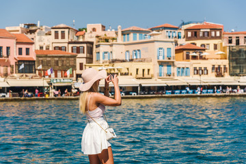 Fototapeta na wymiar Attractive female tourist/ influencer taking photo with a smartphone during sumer vacation. Chania, Crete, Greece