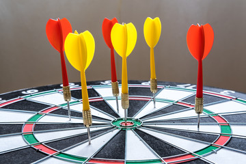 Red and yellow dart arrows hitting in the target center of dartboard. Success hitting target aim...