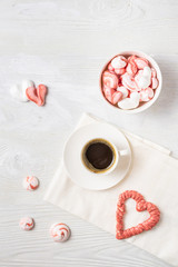 Beautiful romantic breakfast with coffee and meringue cookies in the shape of hearts and candys. White tea-set stand on a wooden table. Flat lay vertical with copy space.