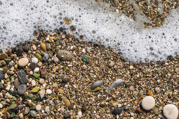 Closeup top view color photography of wet surface of sandy beach with small birght colorful smooth peddles wet from splashing clear salt water of sea waves. Abstract organic photo background. 