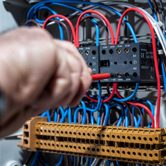 Electrician with screwdriver fixes the cable in a residential electrical distribution panel....