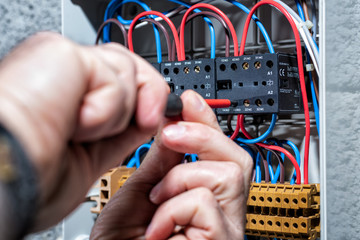 Electrician with screwdriver fixes the cable in a residential electrical distribution panel....