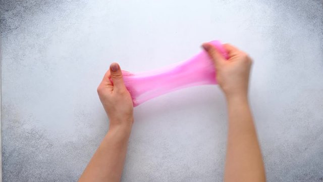 Woman hands playing with pink slime on stone background. Trendy liquid toy. Top view. 4k footage.