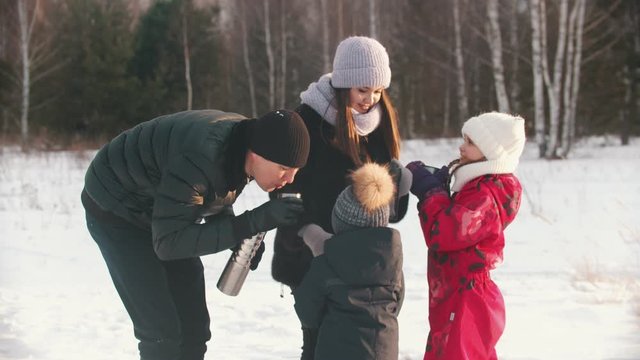 Family of four people drinking hot drinks from the termos in winter time