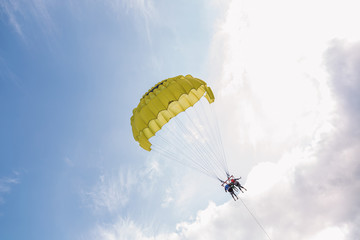 Beach extreme adventures during summer holidays concept. Couple of man and woman flying with yellow parachute over sea water pulled by motorboat. Horizontal color photography.