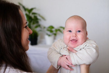 Happy baby. Little cutest chubby caucasian white infant child looking and smiling at camera on mother hands. Family life, moms love, motherhood.