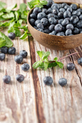 Blueberries in a coconut bowl with mint sprigs are scattered on an old wooden table